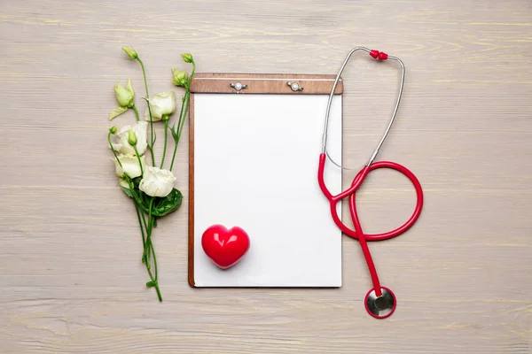 Stethoscope with clipboard, heart and flowers on wooden background — Stock Photo, Image