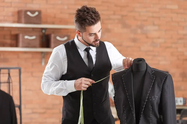 Jeune tailleur prenant des mesures de veste masculine sur mannequin en atelier — Photo