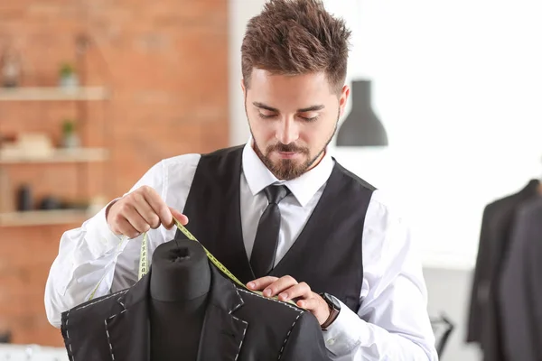 Junge Schneiderin misst männliche Jacke auf Schaufensterpuppe im Atelier — Stockfoto