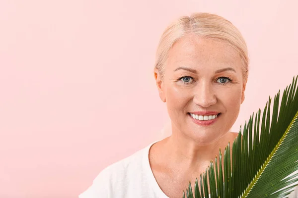 Beautiful mature woman with healthy skin and tropical leaf on color background — Stock Photo, Image
