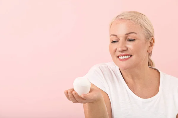 Schöne reife Frau mit Creme auf farbigem Hintergrund — Stockfoto