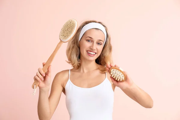 Hermosa joven con cepillos de masaje sobre fondo de color —  Fotos de Stock