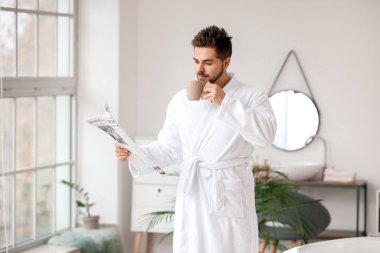 Yakışıklı genç adam banyoda gazete okurken çay içiyor.