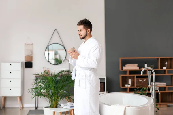 Handsome young man drinking tea in bathroom — Stock Photo, Image