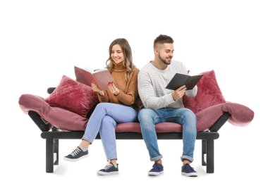 Genç çift beyaz arka planda kanepede otururken kitap okuyor.
