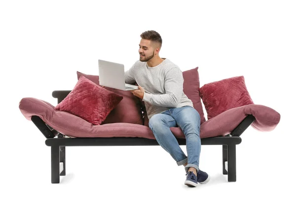 Νεαρός άνδρας με φορητό υπολογιστή κάθεται σε καναπέ σε λευκό φόντο — Φωτογραφία Αρχείου