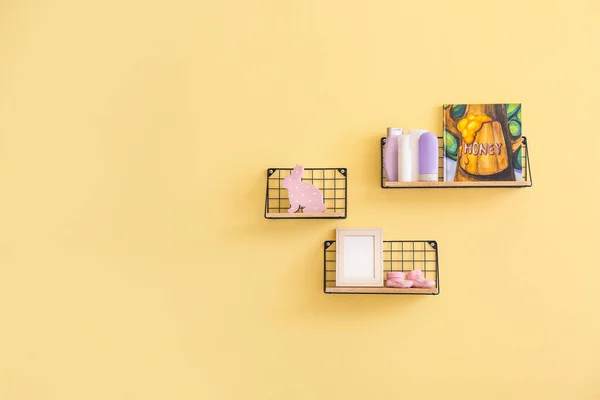 Shelves with baby cosmetics, book and toy on color wall