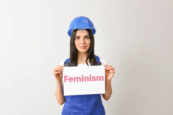 Vrouwelijke werknemer met poster met tekst Feminisme tegen lichte achtergrond — Stockfoto
