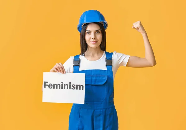 Young woman holding paper with text FEMINISM on color background — Stock Photo, Image