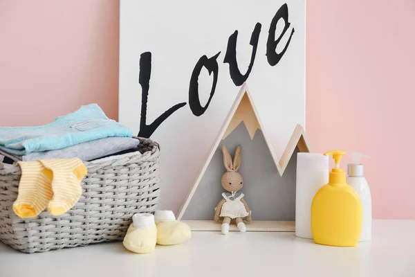 Ropa de bebé con cosméticos y juguete en la mesa en la habitación — Foto de Stock