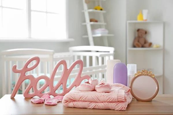 Baby clothes with cosmetics on table in room — Stock Photo, Image
