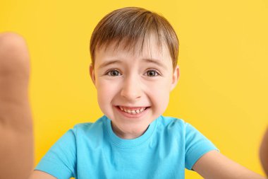 Happy smiling little boy taking selfie on color background
