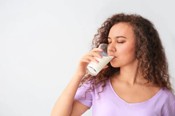 Young African-American woman with milk on grey background — Stock Photo, Image