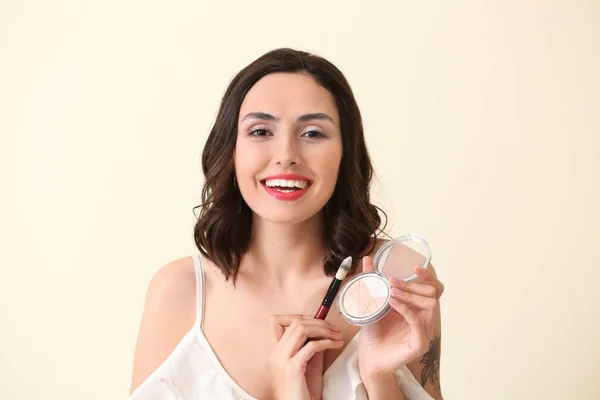 Beautiful young woman applying makeup on light background — Stock Photo, Image