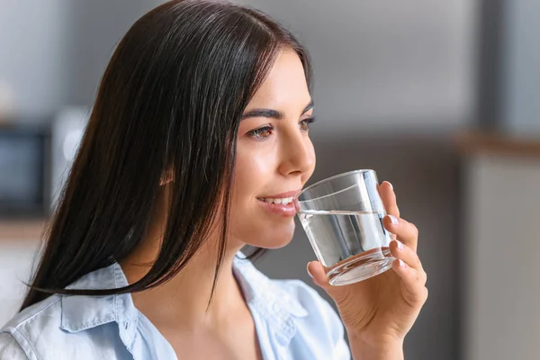 Beautiful young woman drinking water in kitchen — Stock Photo, Image