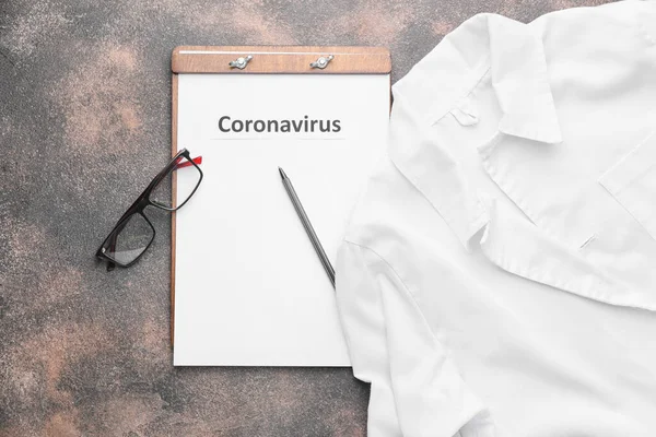 Hoja de papel con texto "Coronavirus" y uniforme médico sobre fondo gris — Foto de Stock