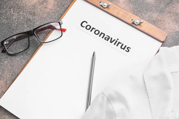 Hoja de papel con texto "Coronavirus" y uniforme médico sobre fondo gris — Foto de Stock