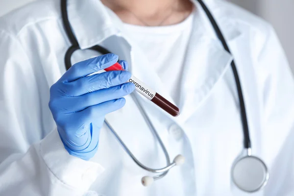 Female doctor holding blood sample in test tube with text CORONAVIRUS, closeup — Stock Photo, Image