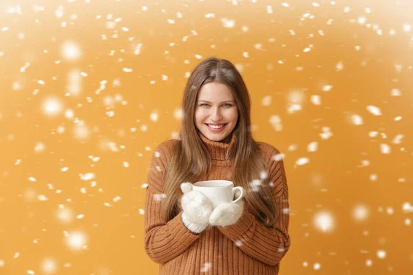Красивая молодая женщина с горячим кофе и падающим снегом на фоне цвета — стоковое фото