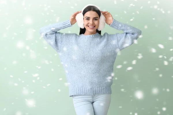 Beautiful young woman in warm sweater and falling snow on color background — Stock Photo, Image