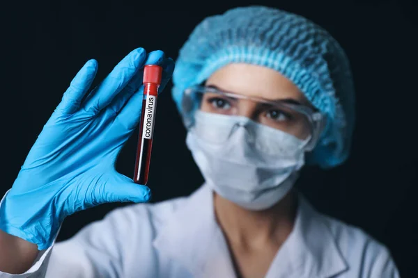 Female doctor holding blood sample in test tube with text CORONAVIRUS on dark background — Stock Photo, Image