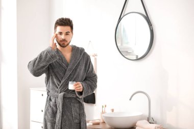 Yakışıklı genç adam banyoda yüzüne krem sürüyor.