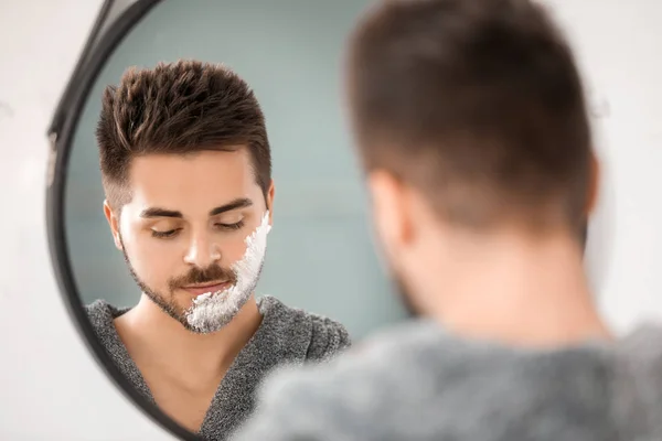 Handsome young man shaving near mirror in bathroom — Stock Photo, Image