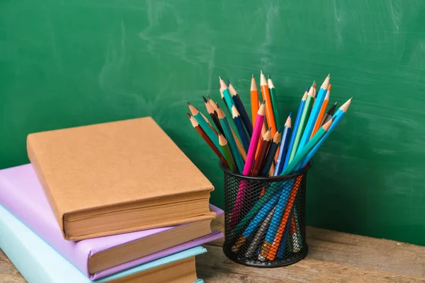 Pencils and books on table near school blackboard — Stock Photo, Image