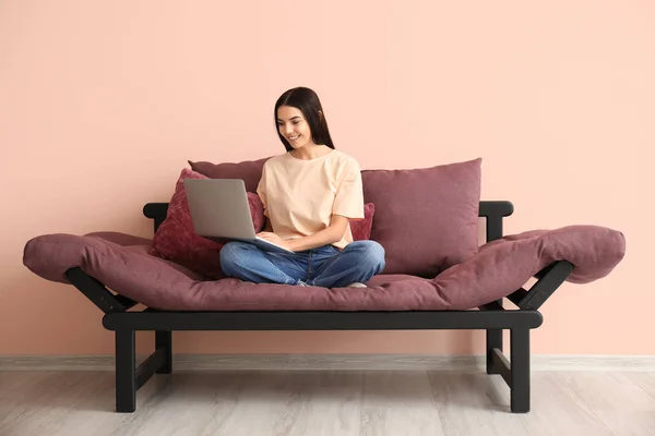 Young woman with laptop sitting on sofa at home — Stock Photo, Image