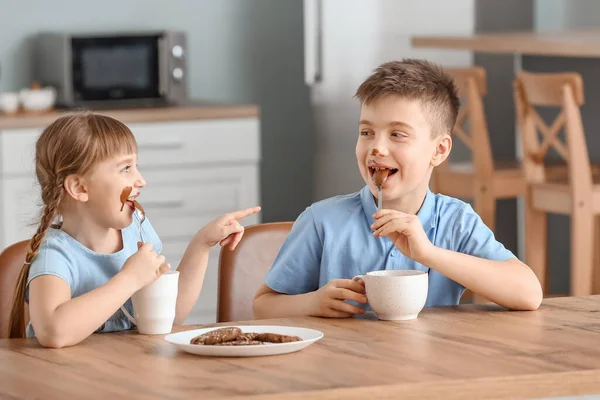 Cute little children eating melted chocolate in kitchen — Stock Photo, Image