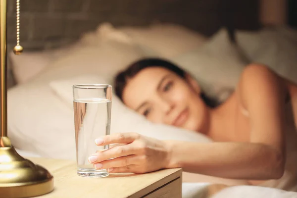 Beautiful young woman taking glass of water from bedside table in evening — Stock Photo, Image