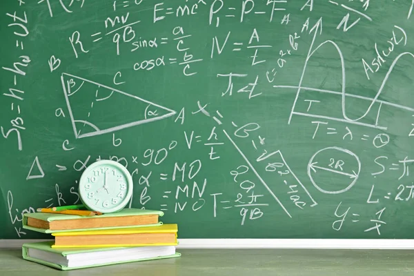 Boeken en klok op tafel bij schoolbord — Stockfoto