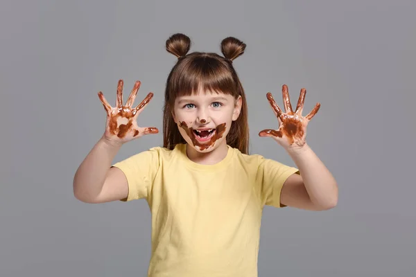 Fetiță drăguță cu ciocolată pe mâini și față pe fundal gri — Fotografie, imagine de stoc