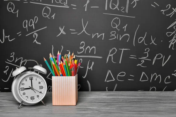 Crayons et horloge sur la table près du tableau noir — Photo