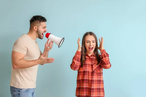 Angry man with megaphone shouting at his wife on color background — Stock Photo, Image