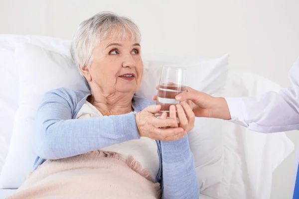 Female doctor giving senior woman suffering from Parkinson syndrome glass of water in clinic — Stock Photo, Image