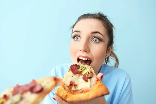 Портрет удивленной молодой женщины, поедающей вкусную пиццу на цветном фоне — стоковое фото