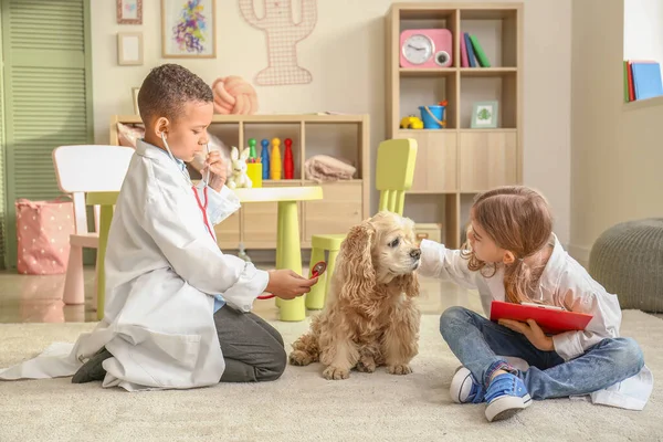 Cute małe dzieci przebrane za lekarzy bawiących się z psem w domu — Zdjęcie stockowe