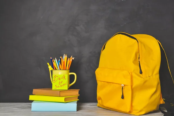 Mochila y juego de útiles escolares en la mesa cerca de pizarra —  Fotos de Stock