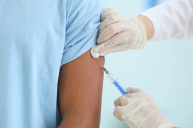Klinikte genç bir çocuğu aşılayan doktor, yakın plan.