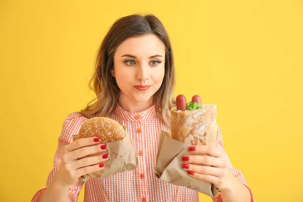 Porträt der schönen jungen Frau mit Burger und französischem Hot Dog auf farbigem Hintergrund — Stockfoto