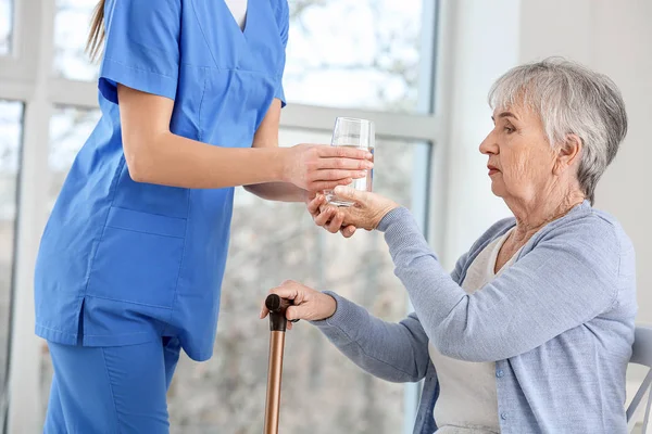 Medico donna che dà donna anziana che soffre di sindrome di Parkinson bicchiere d'acqua in clinica — Foto Stock