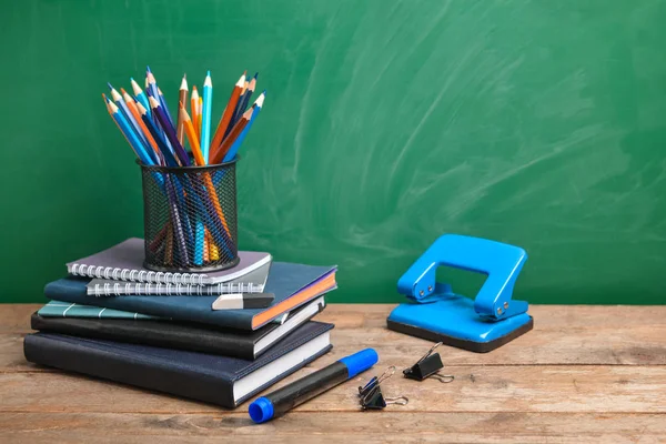 Set of school supplies on table near blackboard — Stock Photo, Image