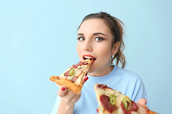 Portrait of beautiful young woman eating tasty pizza on color background — Stock Photo, Image