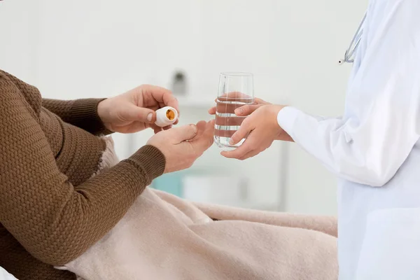 Female doctor helping senior man suffering from Parkinson syndrome to take medicine with water in clinic — Stock Photo, Image