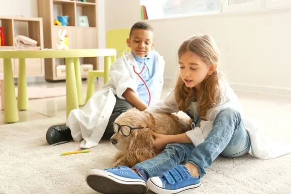 Niedliche kleine Kinder als Ärzte verkleidet, die zu Hause mit Hund spielen — Stockfoto