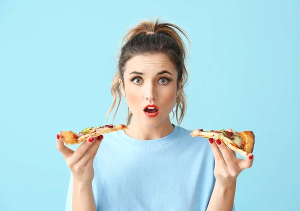 Portrait of surprised young woman eating tasty pizza on color background — 스톡 사진