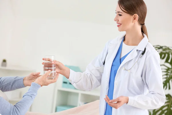 Žena lékař dává starší ženy trpící Parkinsonovým syndromem sklenice vody na klinice — Stock fotografie