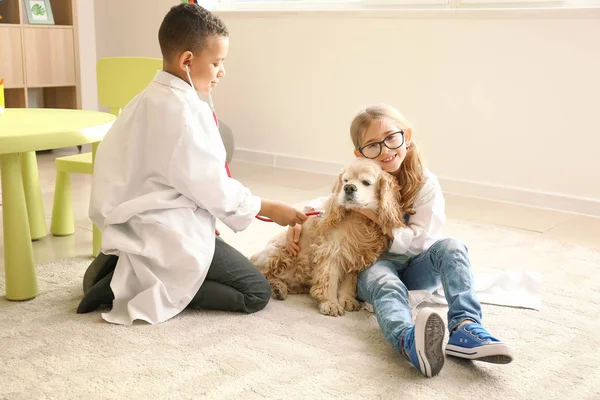Cute little children dressed as doctors playing with dog at home — Stock Photo, Image