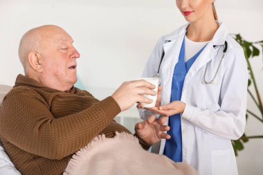 Kadın doktor, klinikte Parkinson sendromu geçiren yaşlı adama çay veriyor.